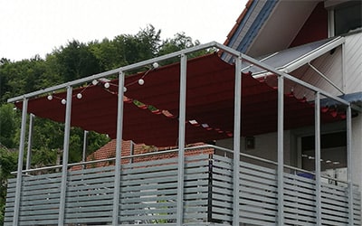 Rotes Raffsegel über einen großen Balkon gespannt